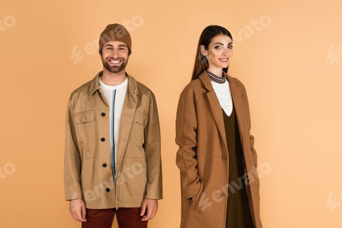Preview: happy couple in trendy autumn clothes looking at camera isolated on beige