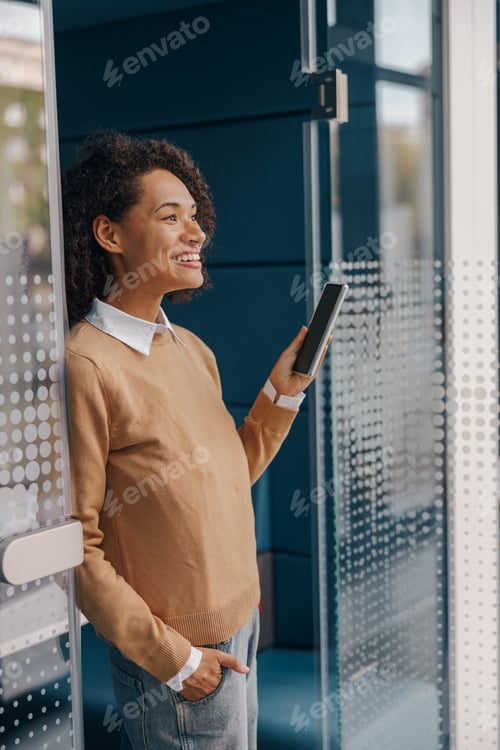 Preview: Smiling woman executive manager is using mobile phone standing in office during break time