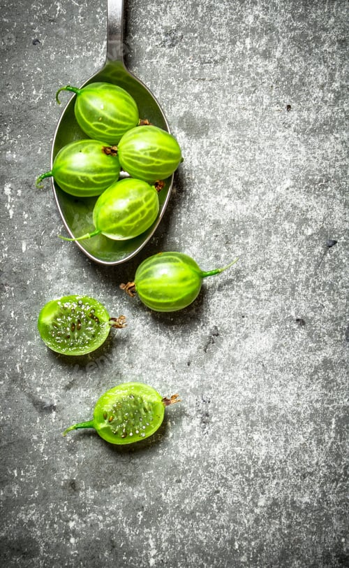 Preview: Green gooseberry in a spoon. On stone background.