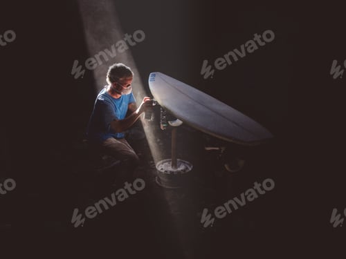 Preview: Man coloring surfboard in dark garage