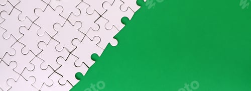 Preview: Fragment of a folded white jigsaw puzzle on the background of a green plastic surface. Texture