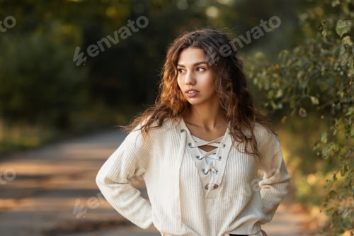 Preview: Cute young curly-haired girl with natural beauty in a knitted sweater walks in the park in nature