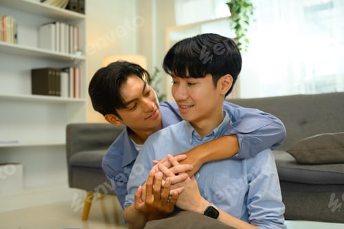 Preview: Loving LGBTQ embracing affectionately and smiling warmly in a cozy living room