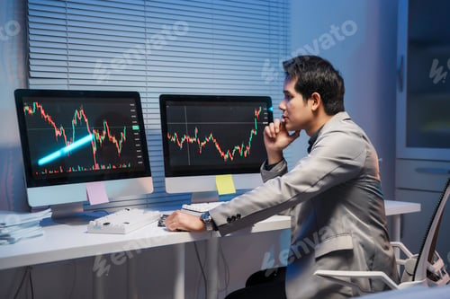 Preview: Stock trader analyzing charts on computer screens in office at night