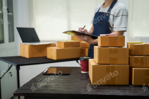 Preview: A man is working at his desk, preparing parcel boxes for shipment.He checks packs items carefully