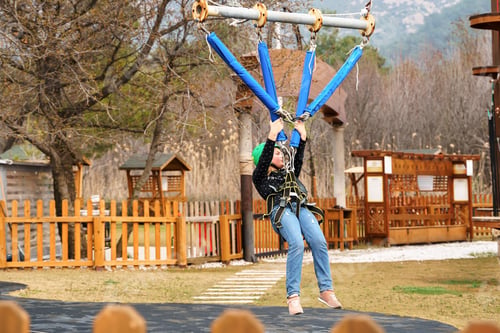 Preview: Teenage teen girl in climbing harness equipment, green sports safety helmet. Rope amusement park.