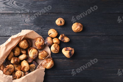 Preview: Paper bag with dried figs on wooden background, top view. Space for text
