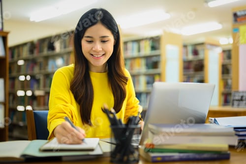 Preview: Beautiful Asian college woman preparing report, doing assignments on laptop in a library.