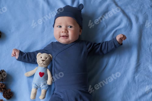 Preview: baby boy 3 months lies and smiles and holds a small toy bear in his hands.