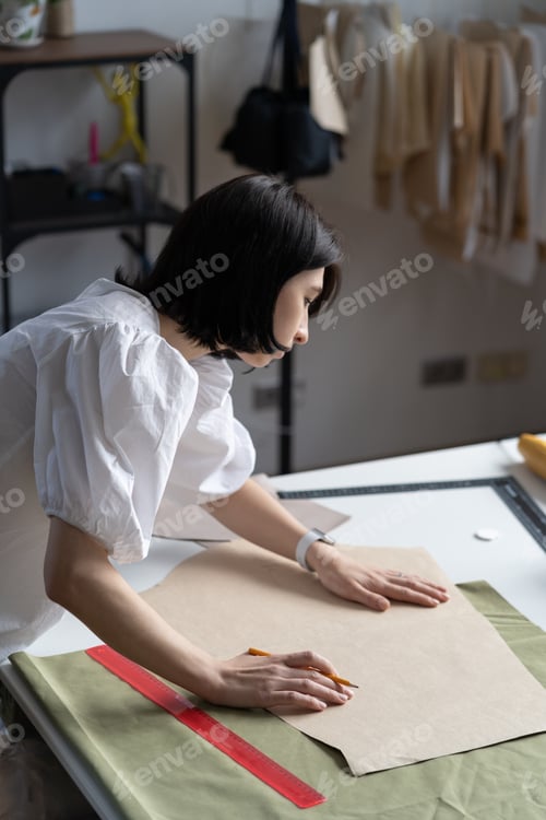 Preview: Young fashion designer in studio work on patterns. Girl dressmaker fit drafts and fabric to sketch