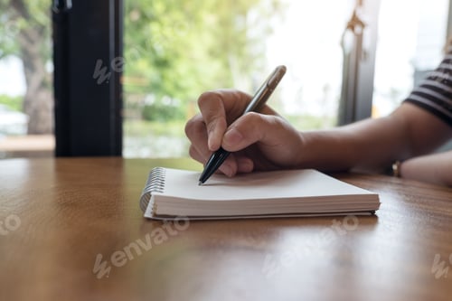 Preview: Closeup image of a woman's hands writing down on a white blank notebook on table