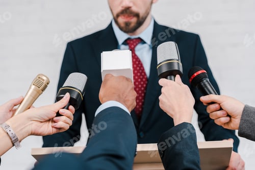 Preview: cropped view of journalists holding microphones near diplomat
