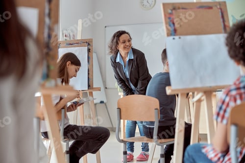 Preview: Smiling happy female mixed race teacher is looking on a pupil's drawing work