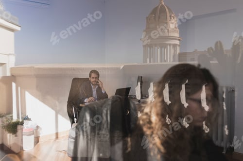 Preview: Serious woman and man talking on smartphone and using laptop at workplaces