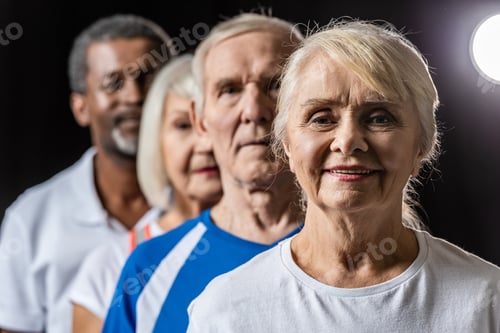 Preview: selective focus of senior woman and her friends looking at camera on black with spotlight