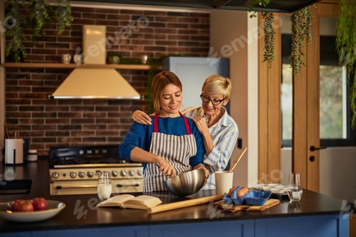 Preview: A mature mother helping her daughter in the kitchen, making a dough.