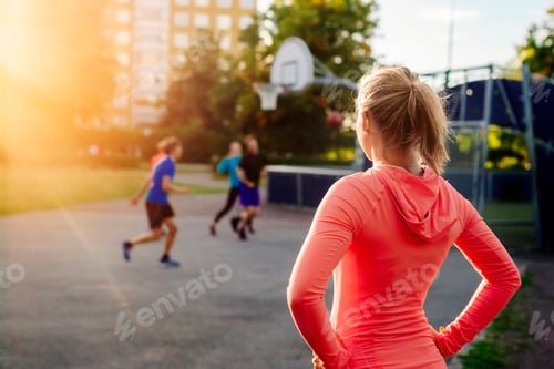 Preview: Rear view of sporty woman looking at friends playing basketball at park