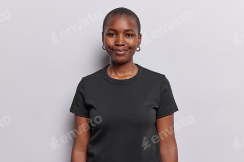 Preview: Portrait of good looking calm woman with dark skin smiles gently has confident pleased expression