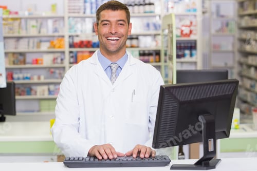 Preview: Male pharmacist standing at pharmacy counter typing on keyboard with shelves of medication