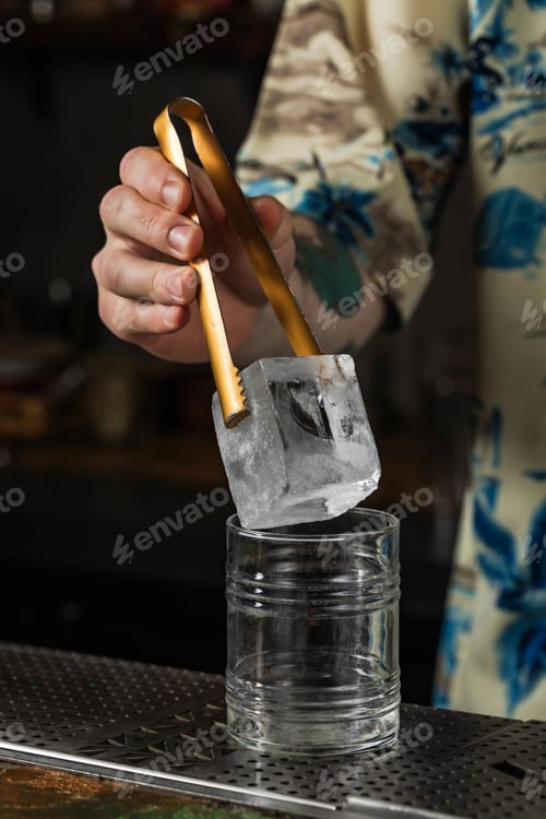 Preview: Bartender putting an ice cube into a rocks cocktail glass with ice tongs