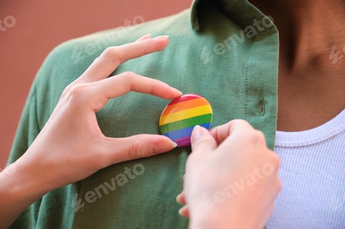 Preview: Woman pinning rainbow badge on a green shirt