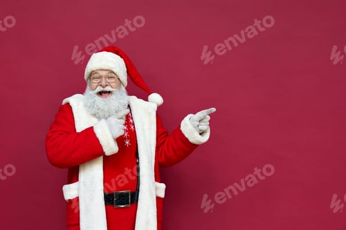 Preview: Happy Santa Claus pointing fingers at copy space advertising on red background.