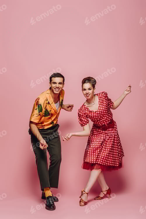 Preview: young dancers looking at camera while dancing boogie-woogie on pink background