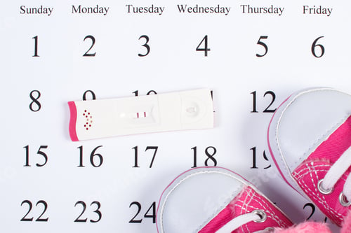 Preview: Pregnancy test with positive result and baby shoes lying on calendar