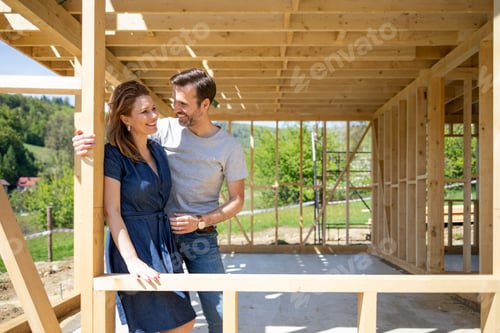 Preview: Couple standing on future window in construction site of their new house, dreams come true