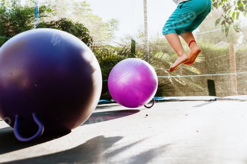 Preview: Boy enjoying his summer vacation jumping on a trampoline at dusk, with a couple of fitness balls.