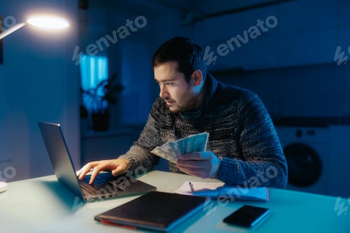 Preview: Bearded man sits at table, counting dollars money and doing evening calculations