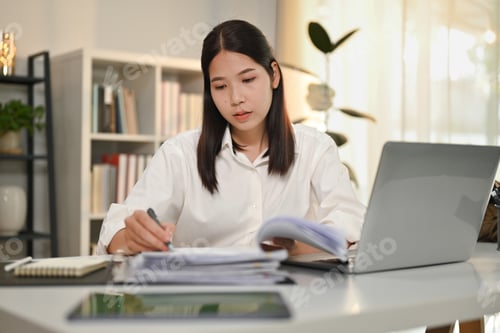 Preview: Attractive female accountant holding pen writing on documents, checking marketing report at desk.