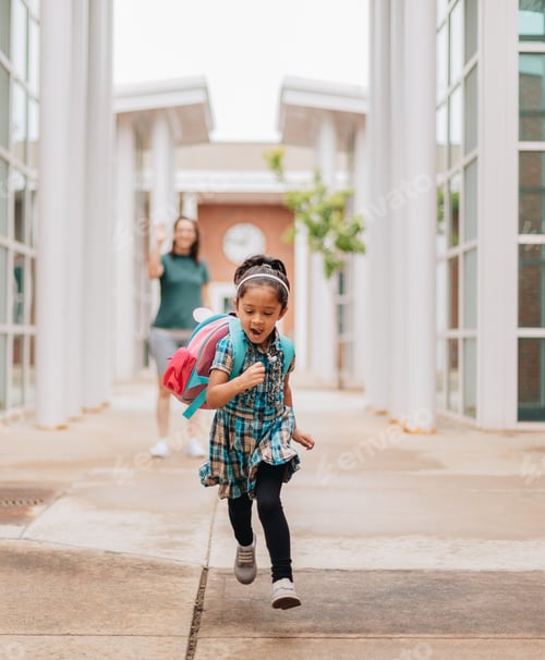 Preview: Mother waving goodbye to preschool daughter who runs towards school building for first day of school