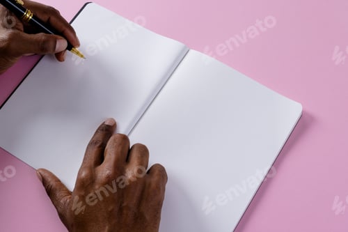 Preview: Hands of biracial man holding pen and writing in notebook with copy space on pink background