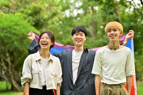 Preview: Image of young people with LGBTQ pride flag, standing in public park.