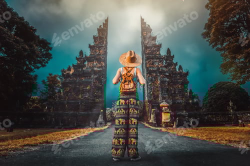 Preview: Woman with backpack walking at big entrance gate in Bali, Indonesia.