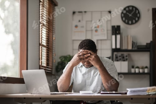 Preview: African American businessman feeling stressed while working using laptop Take notes on documents in