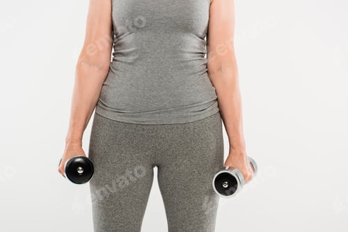Vista previa: cropped view of senior woman in grey sportswear exercising with dumbbells isolated on grey