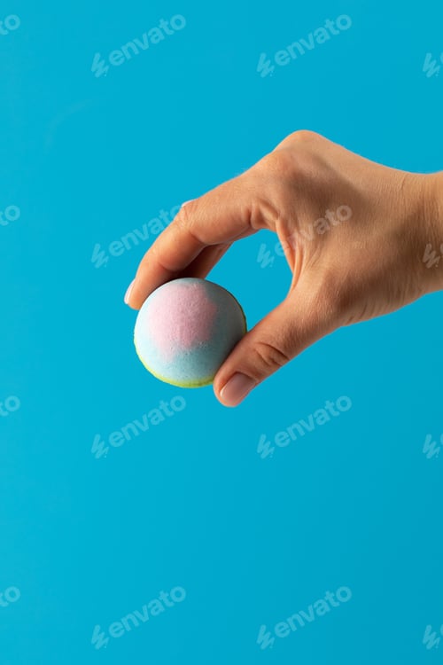 Preview: Woman holds colourful bath bomb carefully on blue background