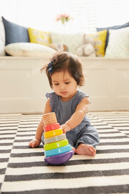 Preview: Baby girl sitting on rug playing with baby toy