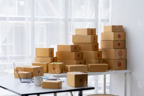 Preview: Parcel boxes on shelf and color shopping bags placing near laptop on table. SME business on shopping