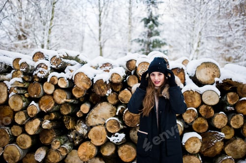 Preview: Beautiful brunette girl in winter warm clothing. Model on winter jacket and hat near stumps trees.