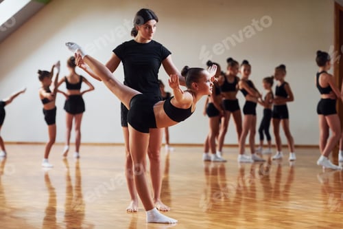 Preview: Woman teaching and helping. Group of female kids practicing athletic exercises together indoors