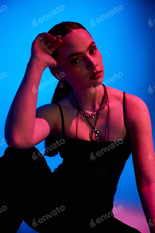 Preview: Stylish young woman poses elegantly against a vibrant blue and pink backdrop