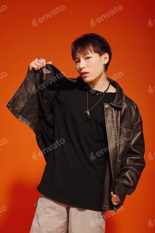 Preview: Stylish young Asian man showcases modern fashion against vibrant orange backdrop