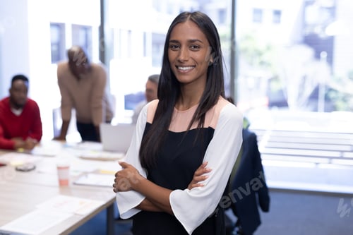 Preview: Portrait of happy african american businesswoman with arms crossed against team in boardroom
