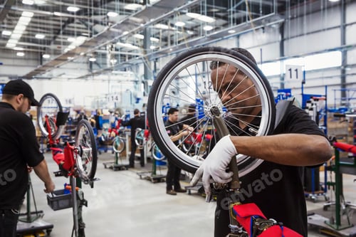 Preview: Male skilled factory worker assembling a bicycle in a factory, attaching a wheel.