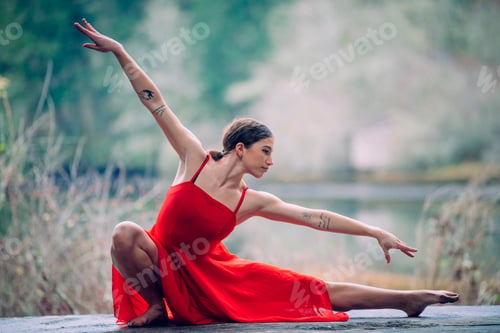 Preview: Woman in a red dress gracefully poses outdoors, extending legs and arms with natural background. USA