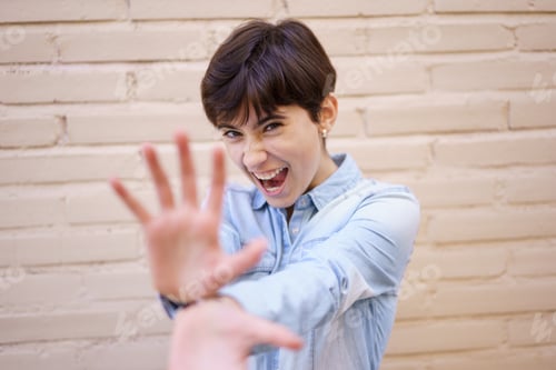 Preview: A Joyful and Cheerful Young Woman Playfully Posing Against a Colorful Brick Wall