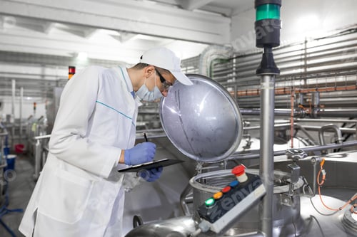 Preview: Inspector in a mask and a scrub stands with a folder-tablet in his hands at the dairy plant